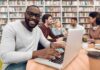 Man smiling while typing on a laptop in a library