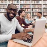 Culture Brawl: LGBTQ Book Sparks Backlash Man smiling while typing on a laptop in a library