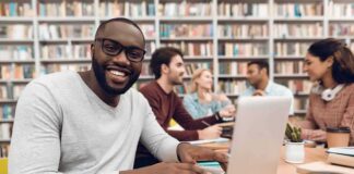 Man smiling while typing on a laptop in a library