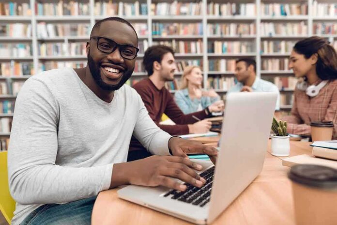 shutterstock_1057976711-1 Man smiling while typing on a laptop in a library