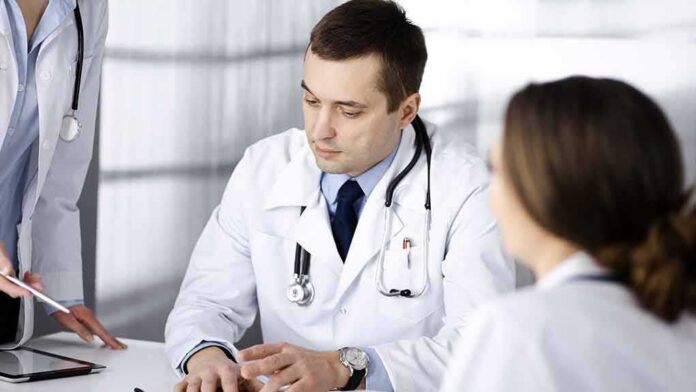 shutterstock_1926064859 Doctors in white coats discuss patient case at a table