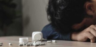 Person with head down near scattered pills on a table