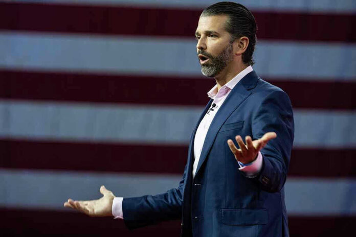 Donald Trump Jr. speaking on stage with arms outstretched