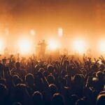 Rock band performing on stage with bright backlights and cheering crowd