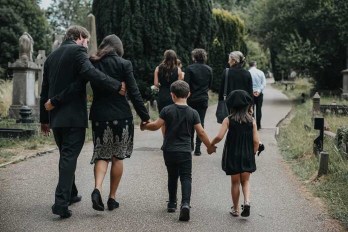 shutterstock_1248435907 Mourners walking together through a cemetery path