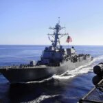 U.S. and Iran Exchange Blows as Military Deaths Continue to Mount naval destroyer sailing at sea with flag flying