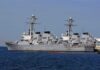 Three gray naval destroyers docked side by side at a pier