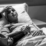 Dementia Often Affects Couples Together, Studies Suggest Patient in hospital bed with nasal oxygen held by visitor
