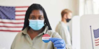 Voter wearing a mask holds an I Voted sticker at a polling place