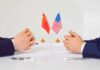 U.S.-China Trade Truce Extended to January 10 Two diplomats sit across table with China and United States flags between them