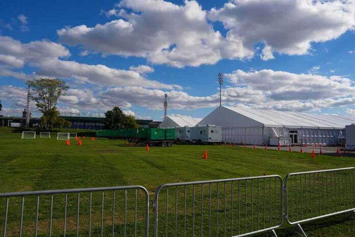 shutterstock_2216173395 Temporary white tents and equipment on a grassy field with traffic cones and metal barriers