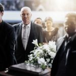 Mourners in formal attire carry a flower-adorned casket indoors