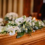Genocide General’s Burial Sparks EU Backlash Coffin with white floral arrangement