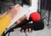 AI Data Centers Spark Voter Backlash Journalist holding two microphones while writing in a notebook