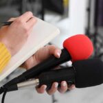 Scientists Track One of Hawaii’s Most Active Volcanic Periods Journalist holding two microphones while writing in a notebook