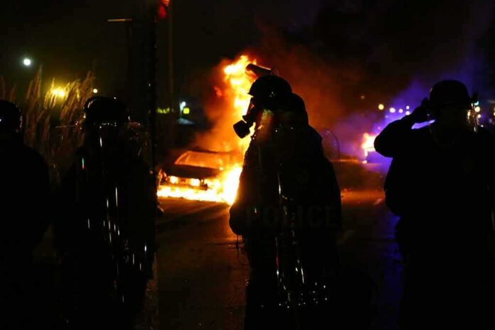 Riot police stand near burning cars at night