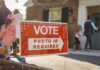 Ballots Offered: Alaska Election System Tested Red voting sign with arrow near people entering a polling place