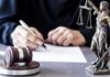 FBI Swoop: Podcaster Indicted Over Trump Threats Judge writing at desk with gavel and Lady Justice statue