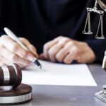 FBI Swoop: Podcaster Indicted Over Trump Threats Judge writing at desk with gavel and Lady Justice statue