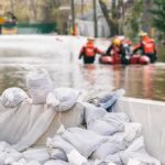 Tropical Storm Bertha Exposes Coastal Risks Sandbags stacked near a flooded street with rescue workers in a boat