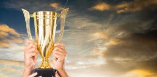 Golden trophy held up by multiple hands at sunset