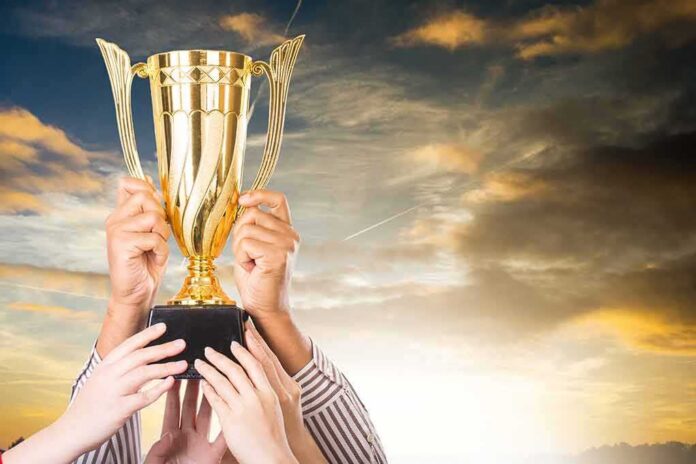 Golden trophy held up by multiple hands at sunset