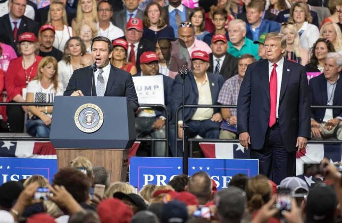 shutterstock_1147142276 Ron DeSantis speaks at a rally podium as Donald Trump stands nearby; Badri Patarkatsishvili in the crowd