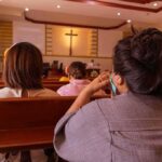 Ecuador Priest Dies in Sudden Church Tragedy people seated in church pews facing a cross