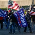 Crowd of people carrying political and American flags at a street gathering