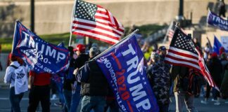 Crowd of people carrying political and American flags at a street gathering