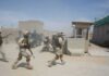 Soldiers in desert uniforms run past a checkpoint amid dust