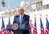 Trump Shifts Funding for Controversial Ads Donald Trump speaking at a podium with American flags and a ship in the background