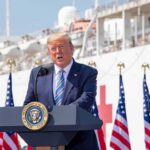 Trump Shifts Funding for Controversial Ads Donald Trump speaking at a podium with American flags and a ship in the background